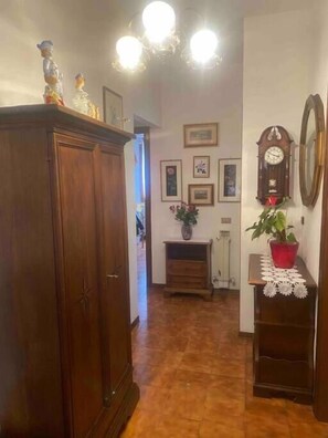 A hallway with a wooden wardrobe, a clock, framed pictures, and a potted plant. - Siena-crete Senesi-val Dorcia (Asciano)