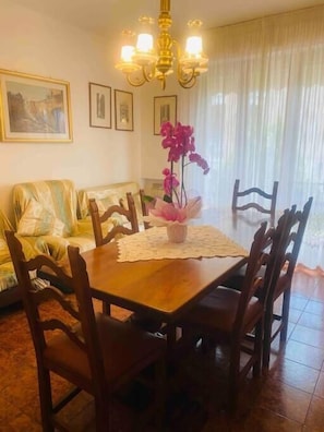 A dining area with a wooden table, chairs, a chandelier, a vase with flowers, and a sofa. - Siena-crete Senesi-val Dorcia (Asciano)