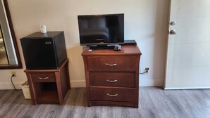 A room with a wooden dresser, a television on top, and a small refrigerator. - Grandview Inn (Surrey)