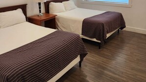 A hotel room with two beds, a nightstand, a lamp, and a window with blinds. - Grandview Inn (Surrey)