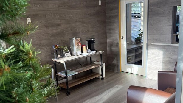 A modern living room with a wooden floor, a brown leather sofa, a coffee table, and a small side table with a coffee maker and a plant. - Grandview Inn (Surrey)