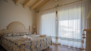 A bedroom with a bed, a nightstand, a lamp, and a window with curtains. - Beautiful Il Giardino Degli Oleandri 1 Bedroom Apartment B2 Sleeps 2 Persons (Arzachena)