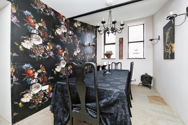 Un comedor con papel tapiz floral negro, una araña y una mesa preparada para cuatro.