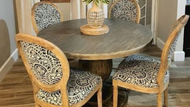 A dining area with a round table, six intricately designed chairs, a hanging light fixture, a potted plant, and a brick wall. - Beach Rustic Condo (Nassau)