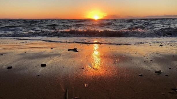Een strand bij zonsondergang, met golven en een heldere lucht.