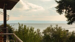 Een uitzicht op een kustgebied met een houten constructie, mogelijk een balkon, dat uitkijkt over de zee en verre bergen.
