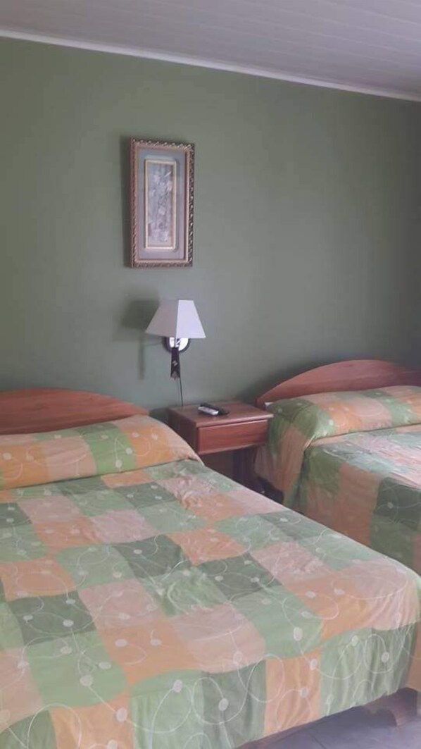 Habitación de hotel con dos camas, una mesita de noche con lámpara y un cuadro enmarcado en la pared.