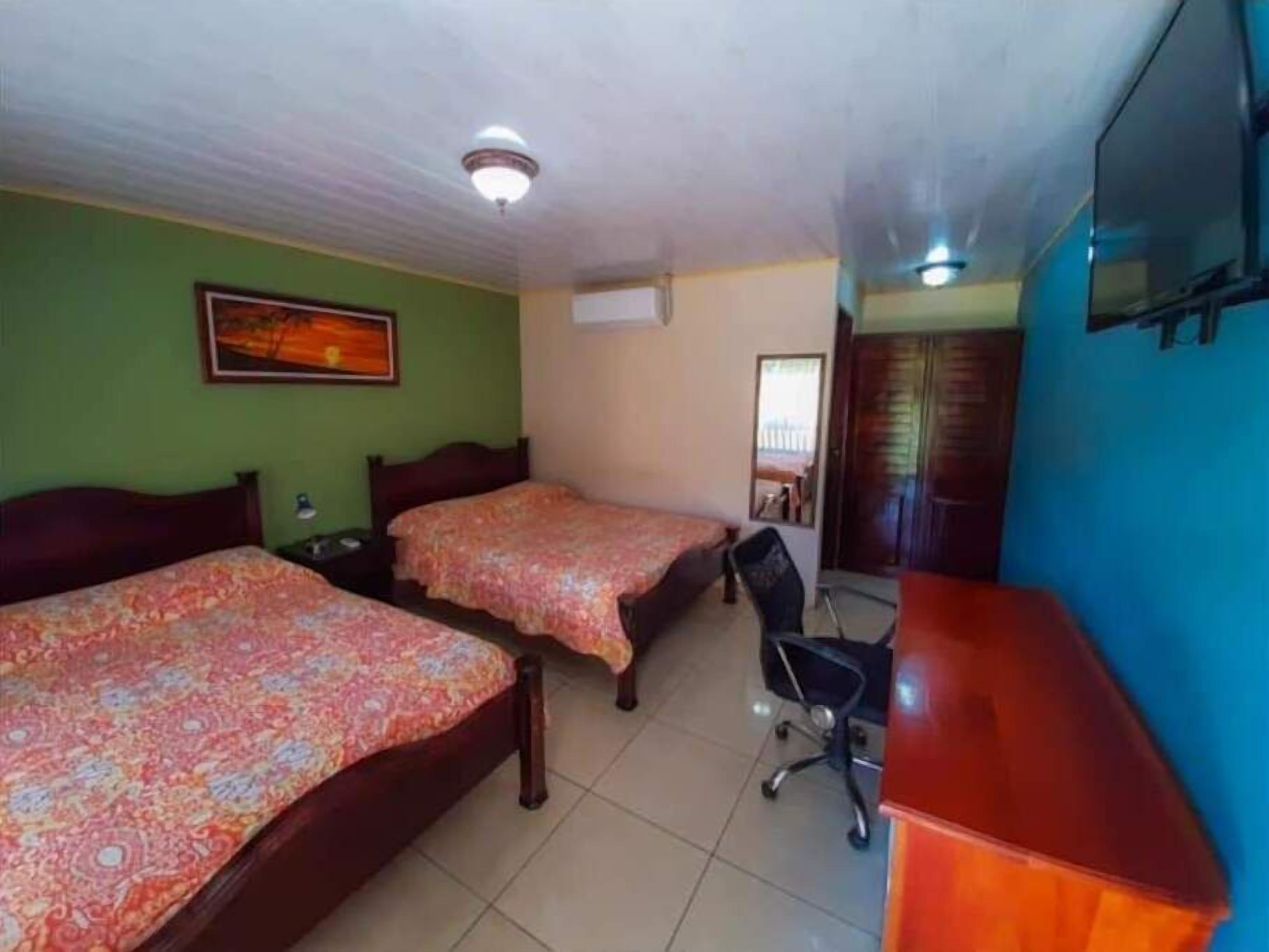 Une chambre avec deux lits, un bureau, une chaise et un ventilateur de plafond.