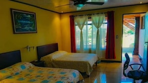 A hotel room with two beds, a ceiling fan, a desk with a chair, and a window with curtains.