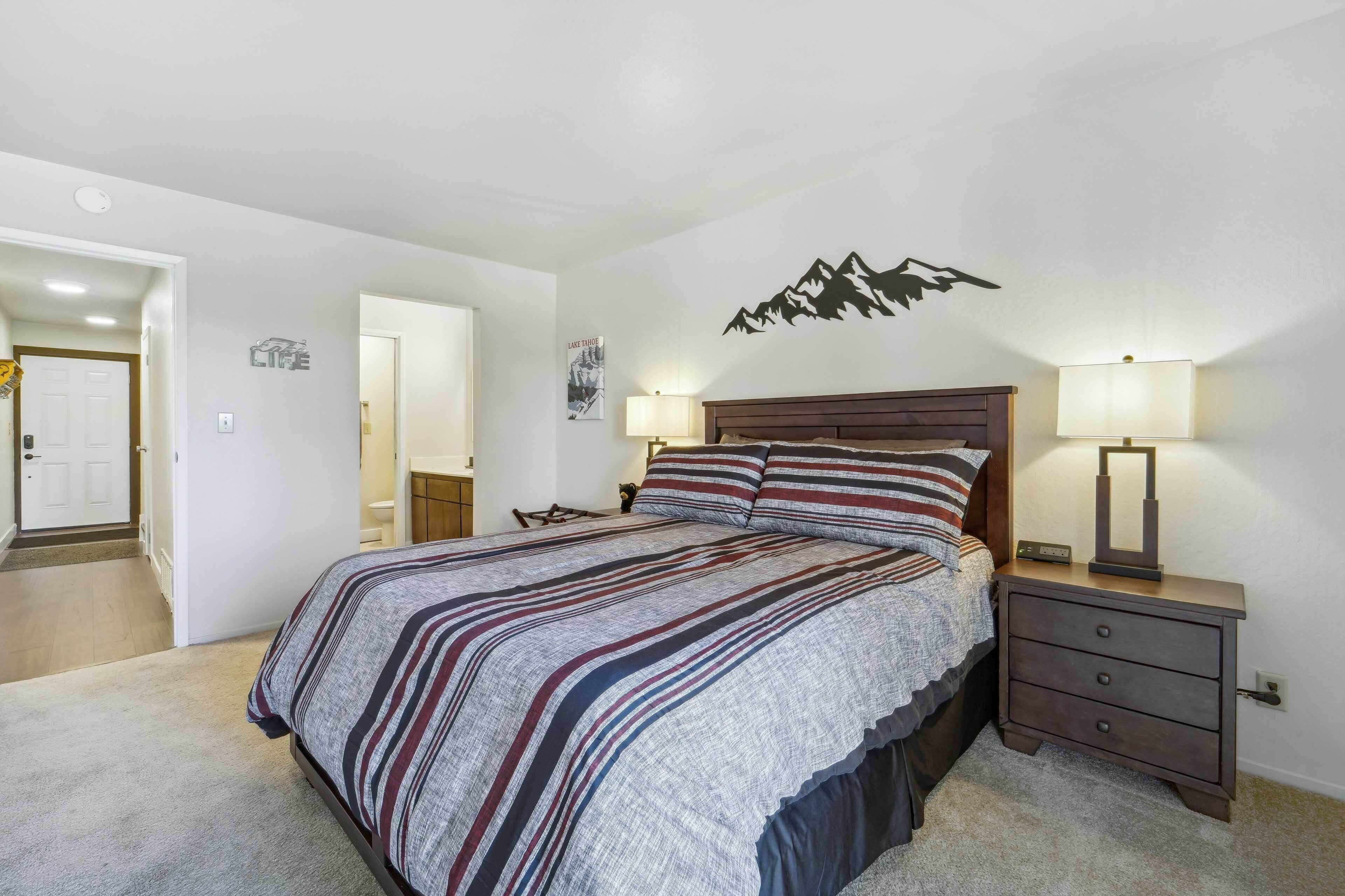 Une chambre à coucher comprenant un lit, deux tables de chevet, une commode et une lampe fixée au mur.