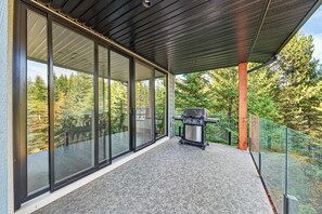 A covered outdoor area with a barbecue grill, glass doors, and a view of trees.