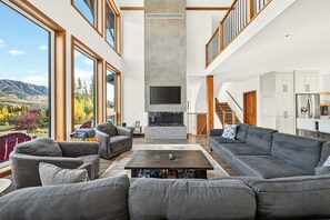 A spacious living room with a fireplace, large windows, and a view of the outdoors. - Fernie Alpine Chalet (Fernie)