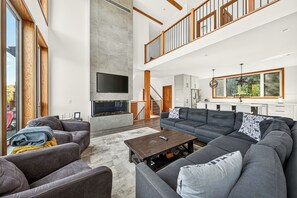 A spacious living room with a large grey sectional sofa, a flat-screen TV mounted on a wall, and a fireplace. - Fernie Alpine Chalet (Fernie)