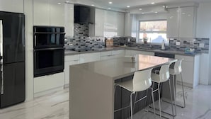 Eine moderne Küche mit weißen Schränken, einem schwarzen Kühlschrank, einem Einbauofen, einer gefliesten Spritzschutzleiste und einer großen Kochinsel mit Barhocker.