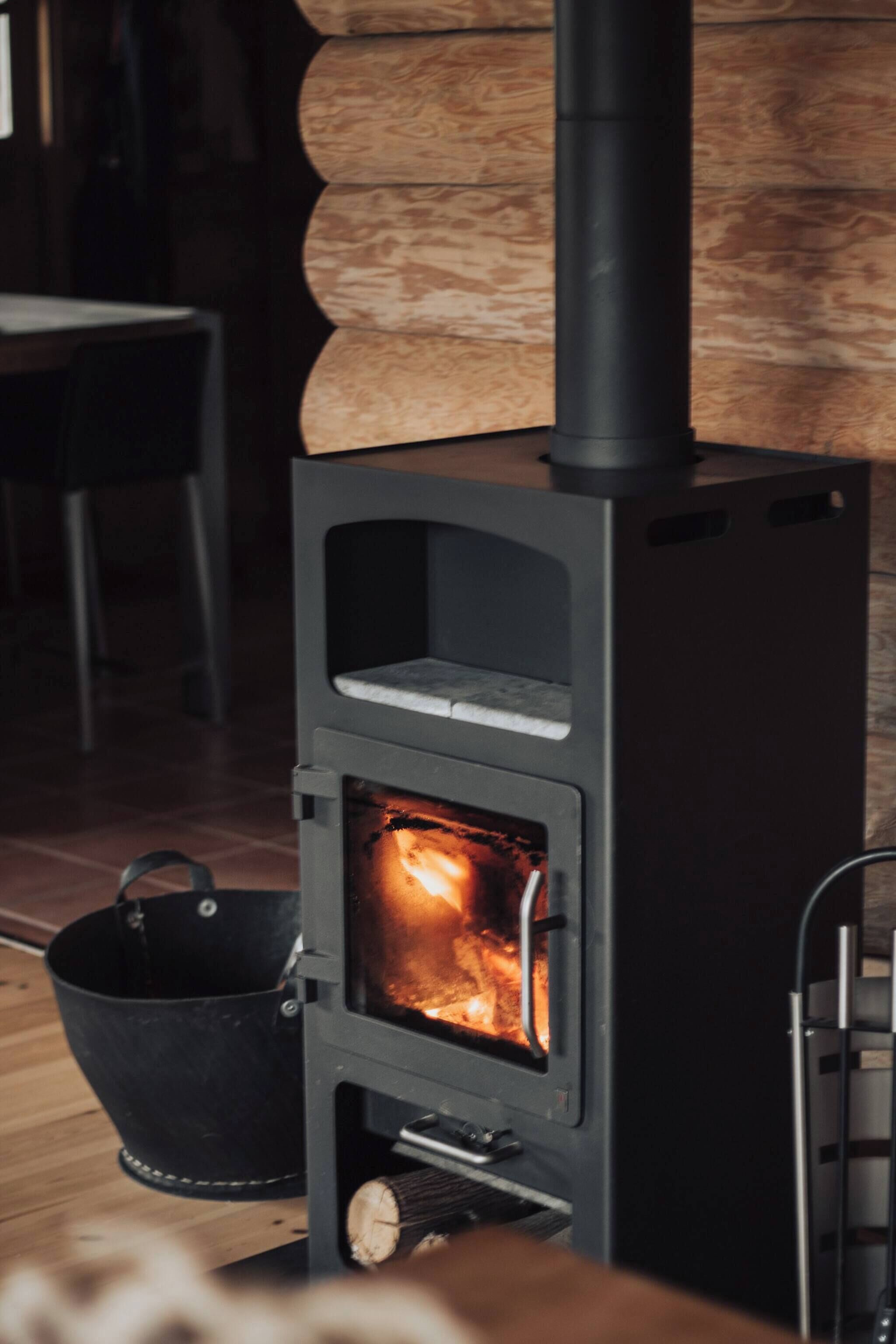 A wood-burning stove with a fire, a black bucket, and a metal rack.