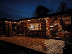 A log cabin with a wooden deck, a large window, and string lights. - Fjordhygge, Cozy Log Retreat Near Sea & Forest - Sauna & Outdoor Living (Jægerspris)