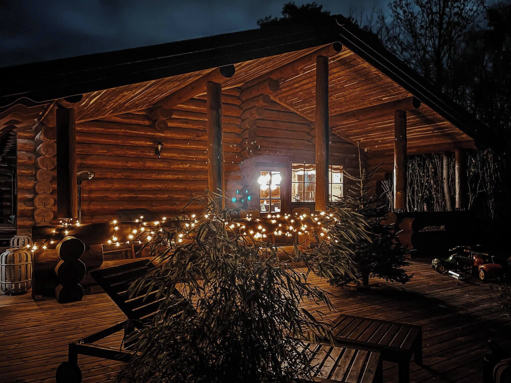 A log cabin with a wooden deck, a bench, and string lights.