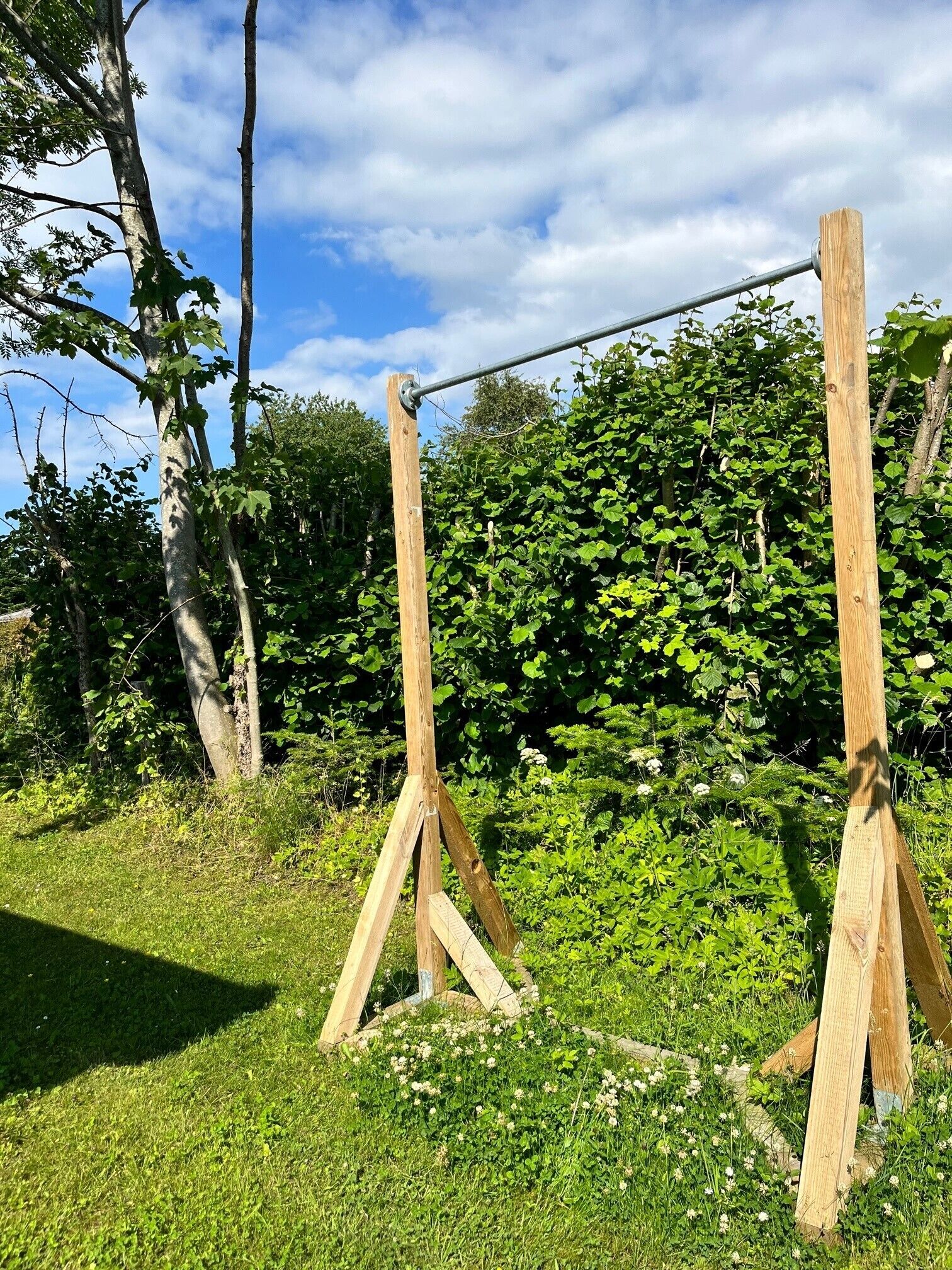 A wooden swing set in a grassy area with trees and a hedge in the background.