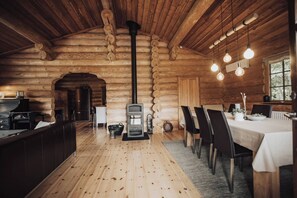 L’intérieur d’une cabane en rondins présente un poêle à bois central, un coin repas avec des chaises et une table, ainsi qu’une cuisine équipée d’un réfrigérateur et d’un évier.