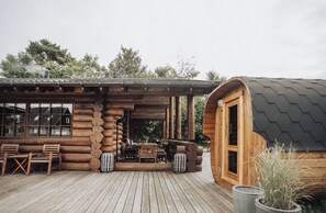 A log cabin with a porch, wooden furniture, and a hexagonal structure. - Fjordhygge, Cozy Log Retreat Near Sea & Forest - Sauna & Outdoor Living (Jægerspris)
