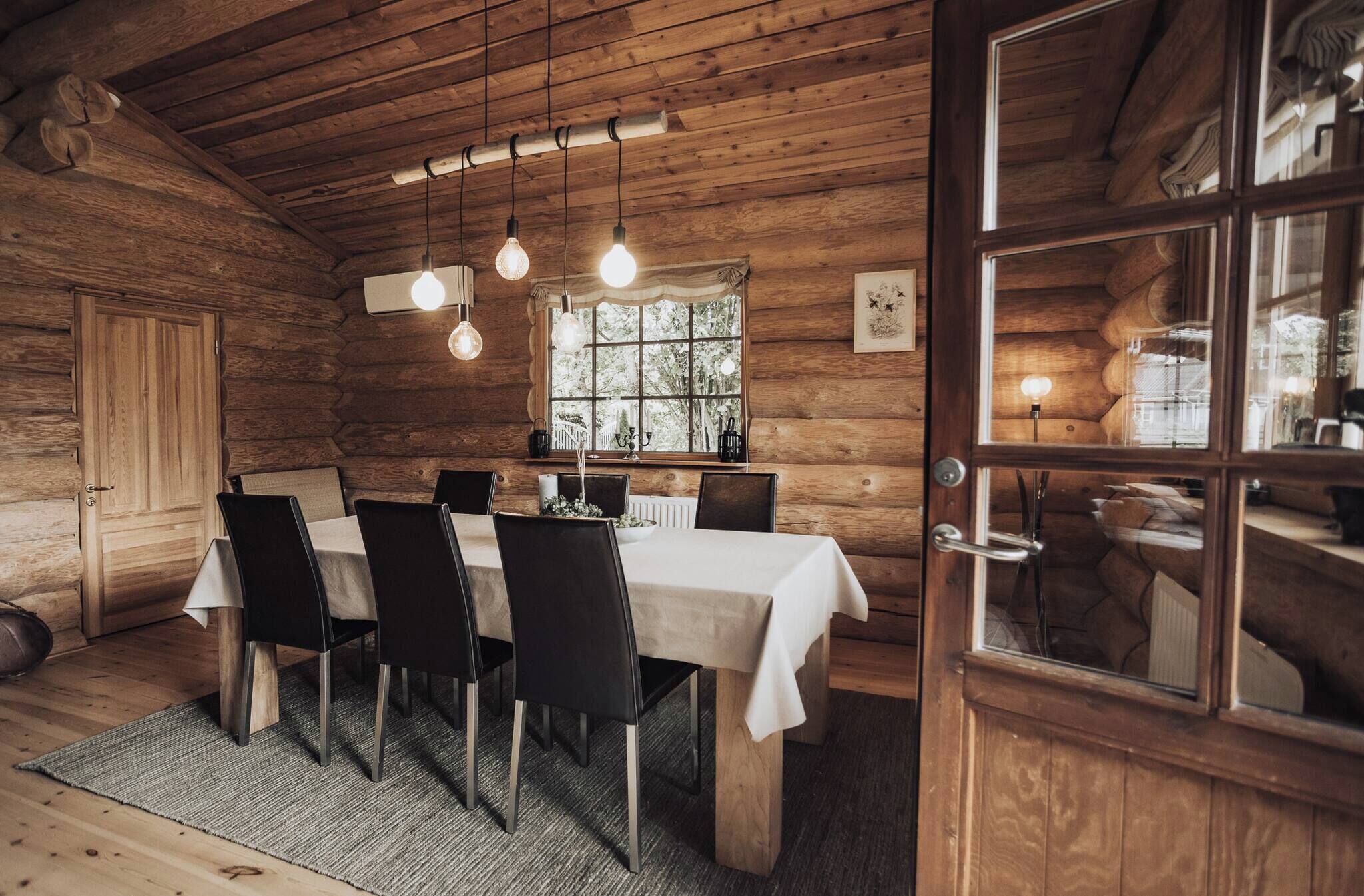 Een houten chalet interieur met een eettafel, stoelen, hangende lampen, een raam en een deur.