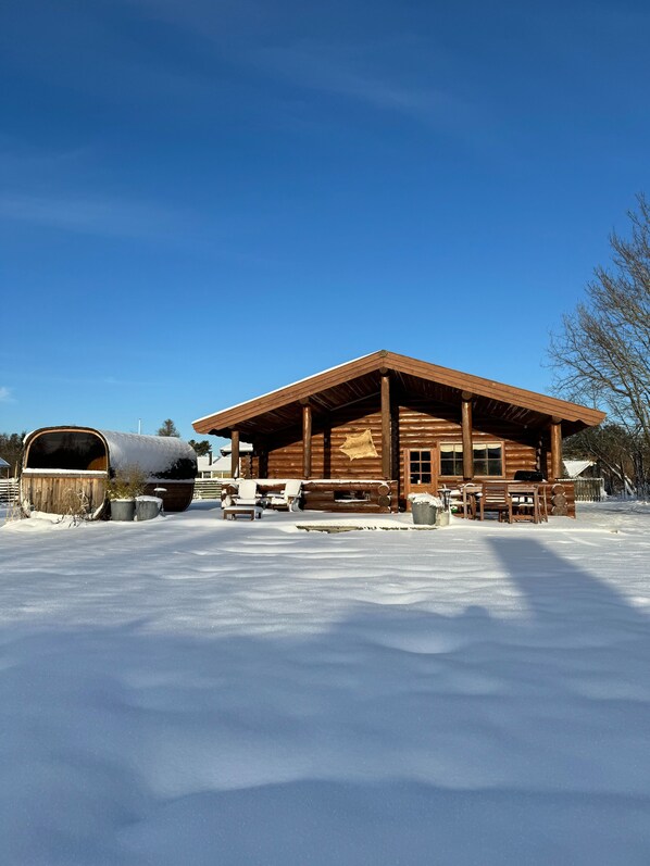 A log cabin with a covered porch, a snow-covered ground, and a clear blue sky. - Fjordhygge, Cozy Log Retreat Near Sea & Forest - Sauna & Outdoor Living (Jægerspris)