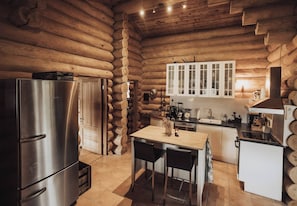 A log cabin interior with a stainless steel refrigerator, wooden cabinets, a wooden dining table, and a kitchen counter. - Fjordhygge, Cozy Log Retreat Near Sea & Forest - Sauna & Outdoor Living (Jægerspris)