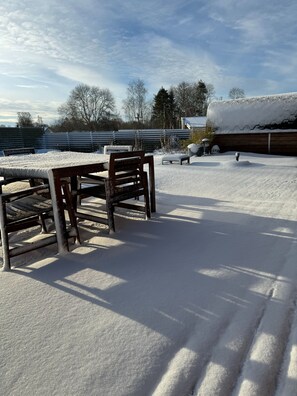 A snow-covered outdoor area with a table and chairs, a wooden fence, and a building in the background. - Fjordhygge, Cozy Log Retreat Near Sea & Forest - Sauna & Outdoor Living (Jægerspris)