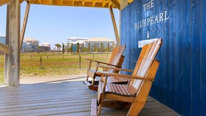A wooden deck with two Adirondack chairs and a blue wall with "THE BLUEPEARL" written on it. - The Blue Pearl · Experience Coastal Living at Blue Pearl: Private Beach Access (Gulf Shores)