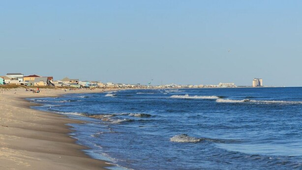 A beach with a clear view of the ocean, sandy shore, and buildings in the background. - The Blue Pearl · Experience Coastal Living at Blue Pearl: Private Beach Access (Gulf Shores)