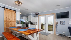 A modern kitchen with a wooden table, white cabinets, and a sliding barn door. - The Blue Pearl · Experience Coastal Living at Blue Pearl: Private Beach Access (Gulf Shores)