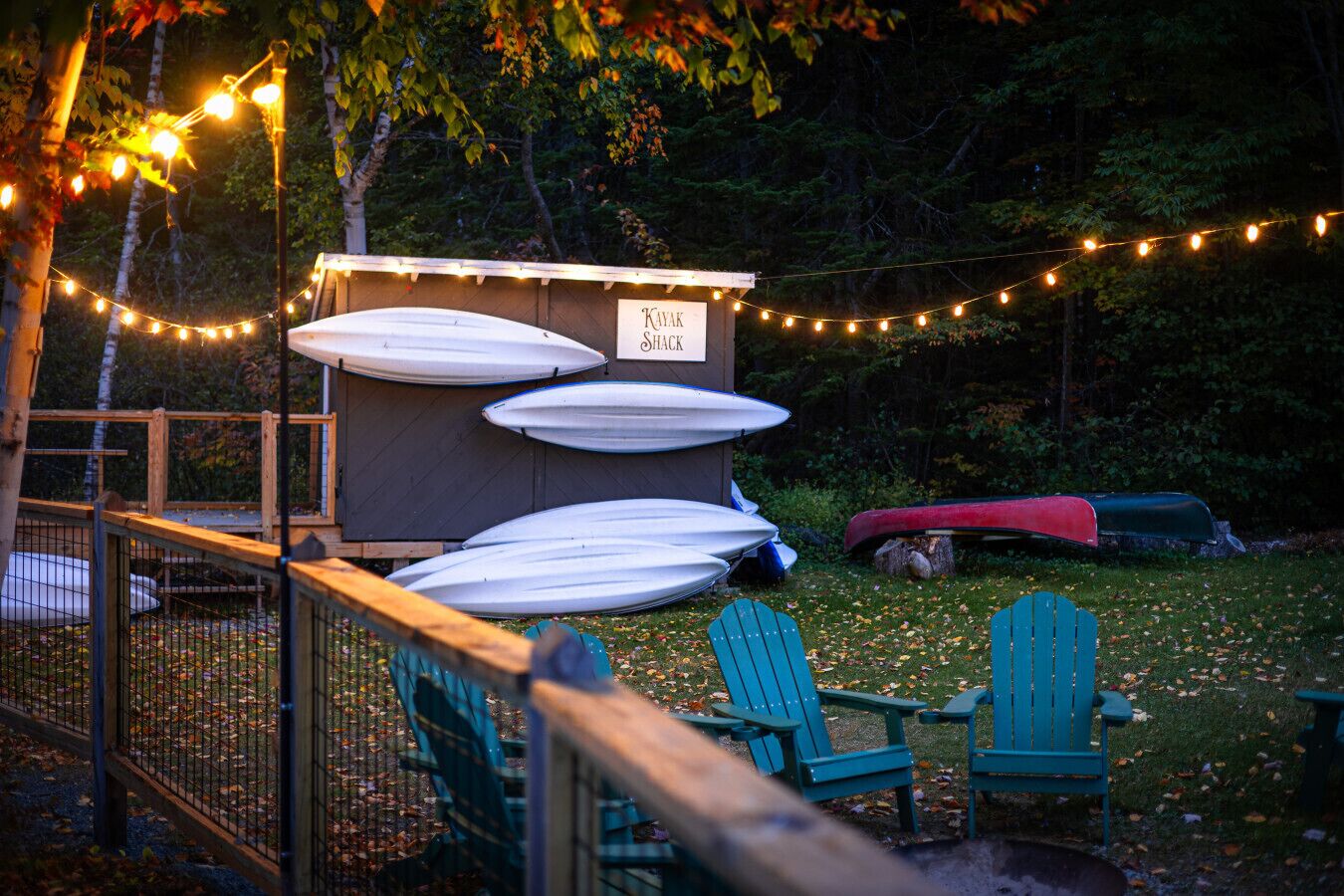 Un cobertizo para kayaks con varias kayaks guardadas en su interior, rodeado por una terraza de madera y una guirnalda de luces.