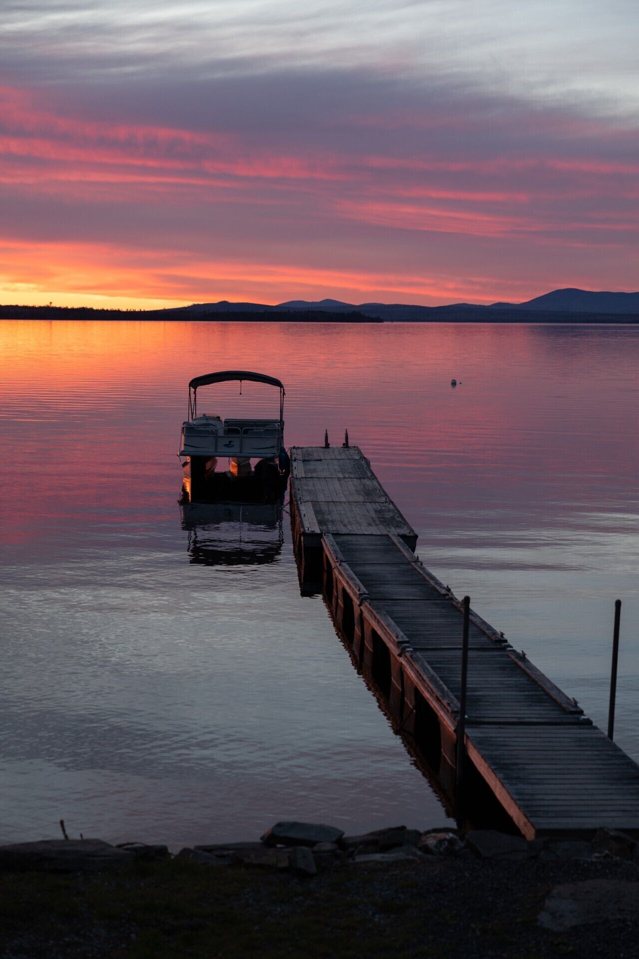 A dock extending into calm water with a vehicle parked at the end.