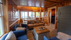 Un intérieur de chalet chaleureux, avec un revêtement mural en bois, un ensemble de canapés, une table à manger et un coin cuisine.