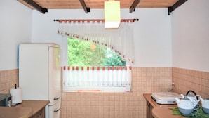 A kitchen with a refrigerator, a stove, and a window with a view of greenery.