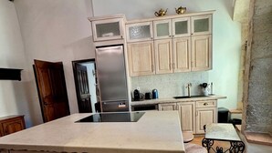 A kitchen with a central island, wooden cabinets, a stainless steel refrigerator, and a chandelier. - Historic Maison du Roy/Royal Chambers -3BR/2BR Apartment with Royal Fireplace (Saint-Antonin-Noble-Val)