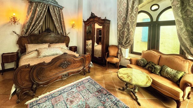 A bedroom with a four-poster bed, a chandelier, a mirror, a sofa, and a patterned rug. - Historic Maison du Roy/Royal Chambers -3BR/2BR Apartment with Royal Fireplace (Saint-Antonin-Noble-Val)