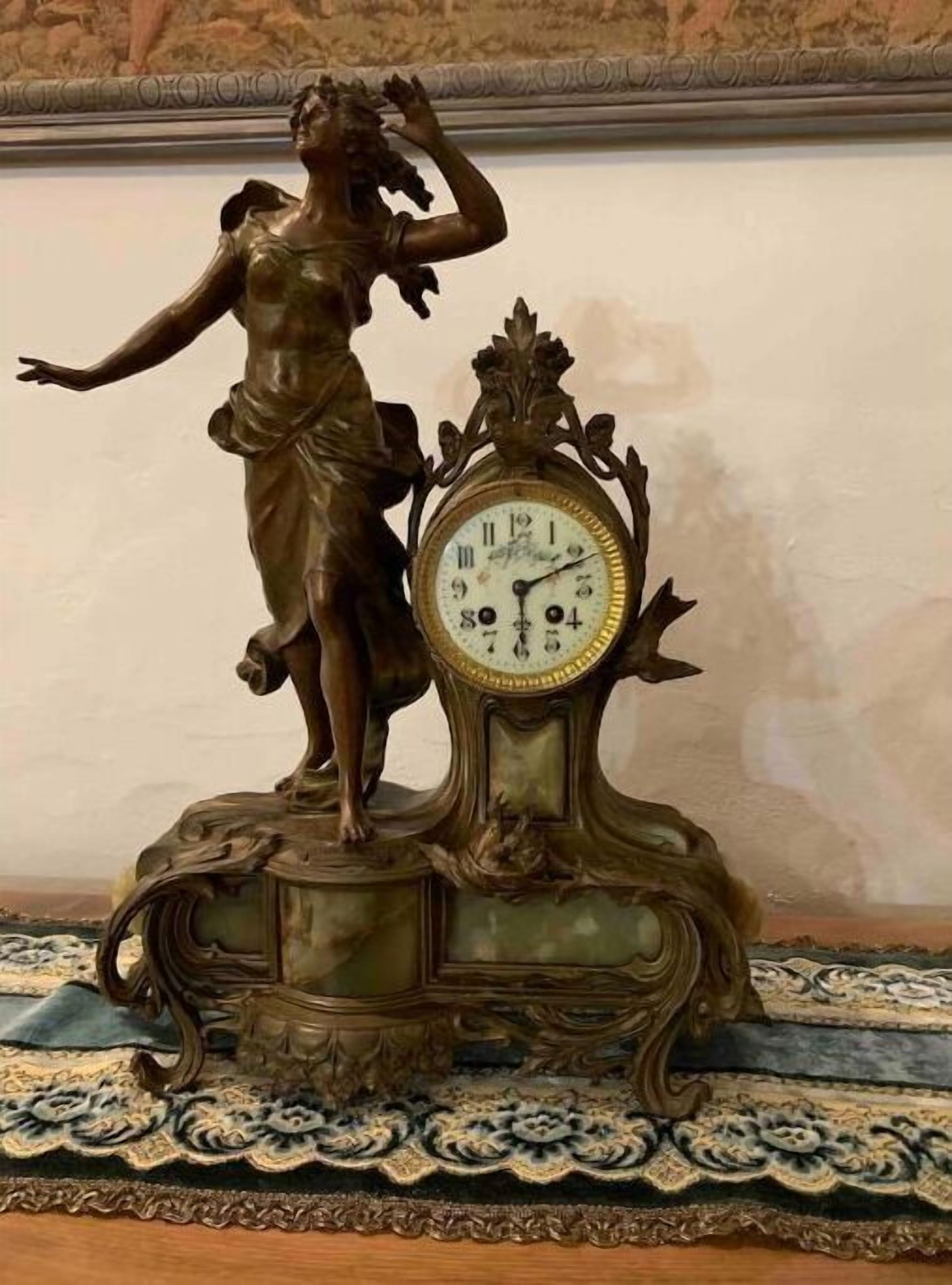 Un reloj con una estatua de una mujer en la parte superior, sobre un base decorativo.