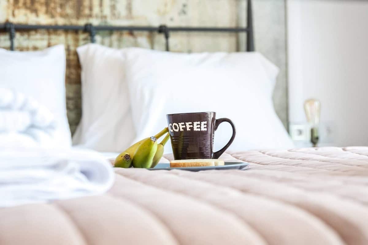 A neatly made bed with a pillow, a mug with 'COFFEE' written on it, and bananas on a tray.