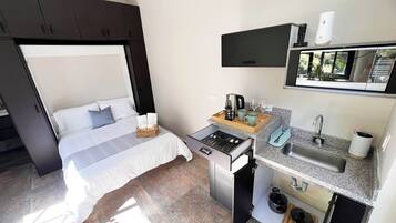 Habitación de hotel pequeña con cama, una kitchenette y un televisor montado en la pared.