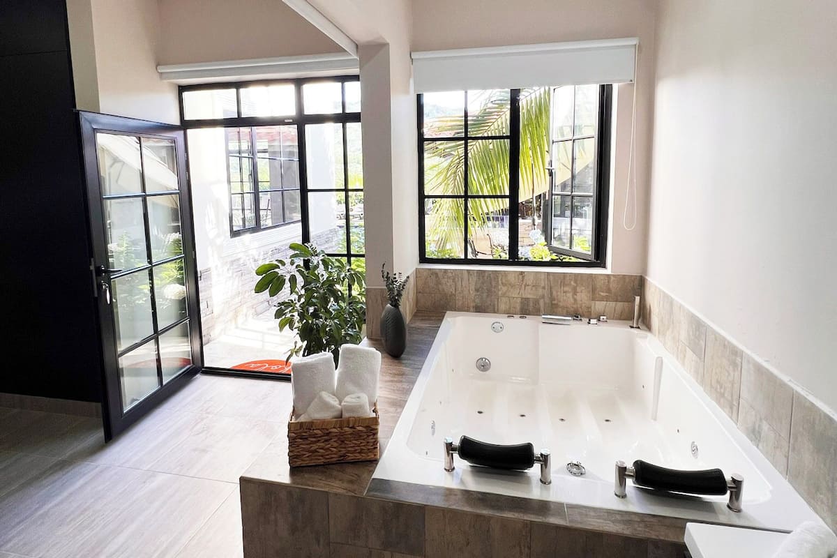 A modern bathroom with a large bathtub, a glass shower enclosure, and large windows offering a view of the outdoors.