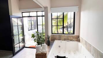 Un baño moderno con una bañera grande, una cabina de ducha de vidrio y amplias ventanas con vistas al exterior.