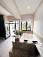 A modern bathroom with a large bathtub, a glass shower enclosure, and large windows offering a view of the outdoors.