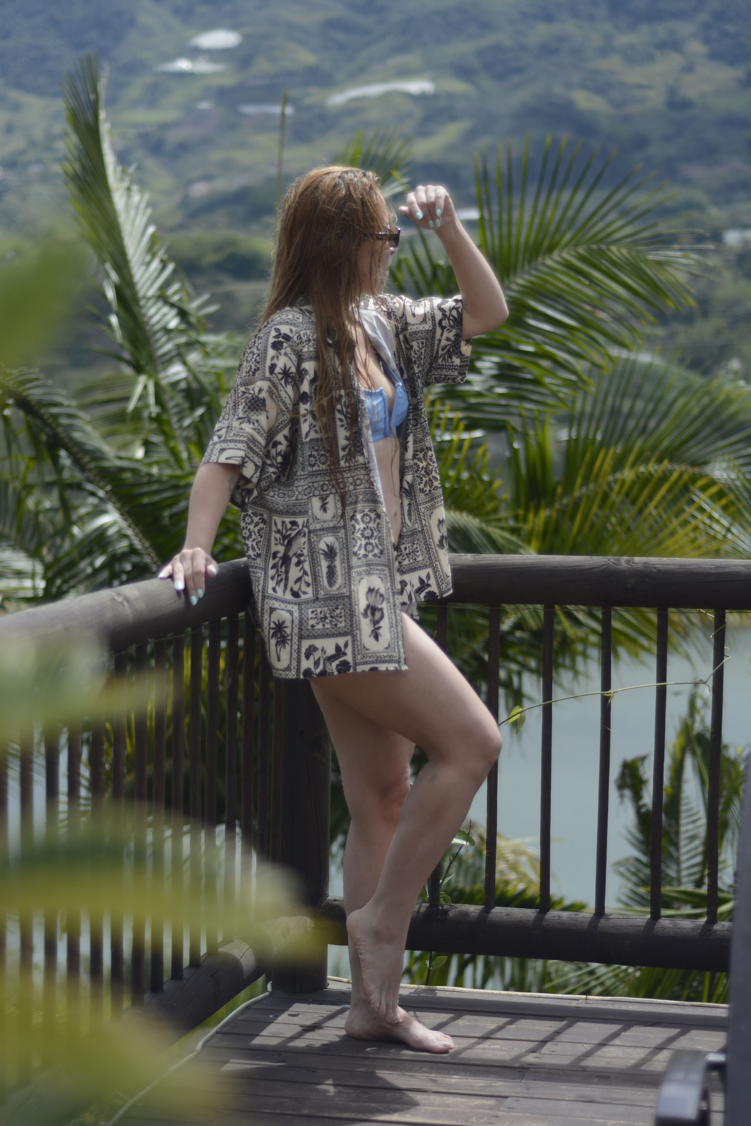 A person standing on a balcony with a view of a lake and palm trees.