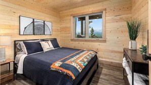 A wooden cabin bedroom with a bed, a window with a view, and a wall-mounted picture. - One of a kind views of Glacier National Park! Cascade Cabin at Thunderbird Ridge. (Polebridge, Montana)