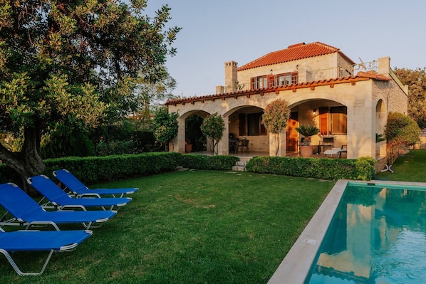 Une villa avec piscine, un patio doté de chaises longues et un jardin.
