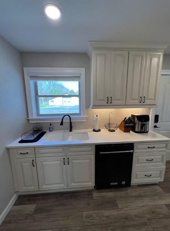 Cocina compacta con armarios blancos, lavavajillas integrado y ventana con vista a un barrio residencial.