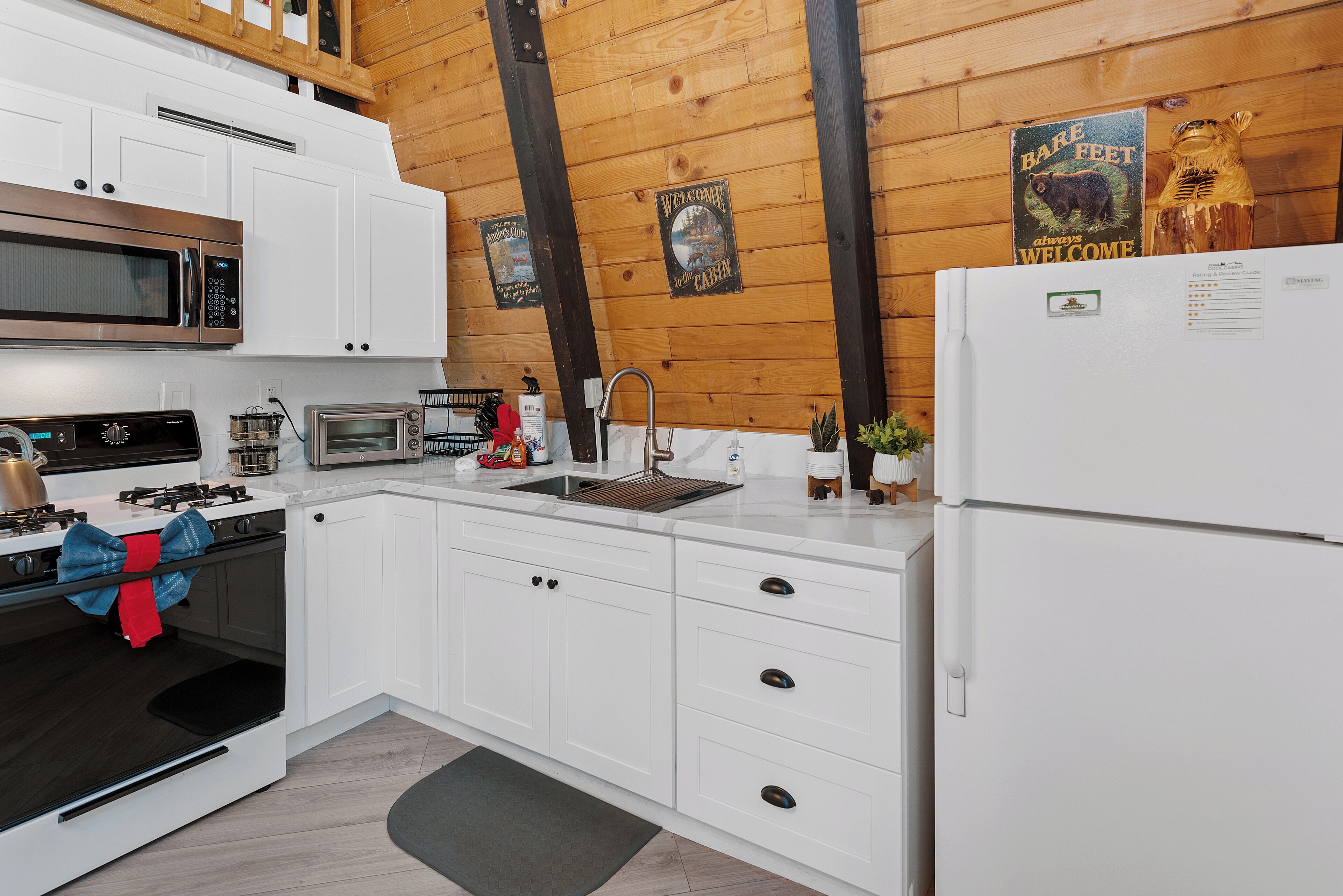 A modern kitchen with white cabinets, a stainless steel microwave, a built-in oven, a sink, and a refrigerator.