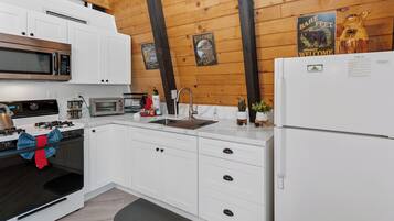 A modern kitchen with white cabinets, a stainless steel microwave, a built-in oven, a sink, and a refrigerator.