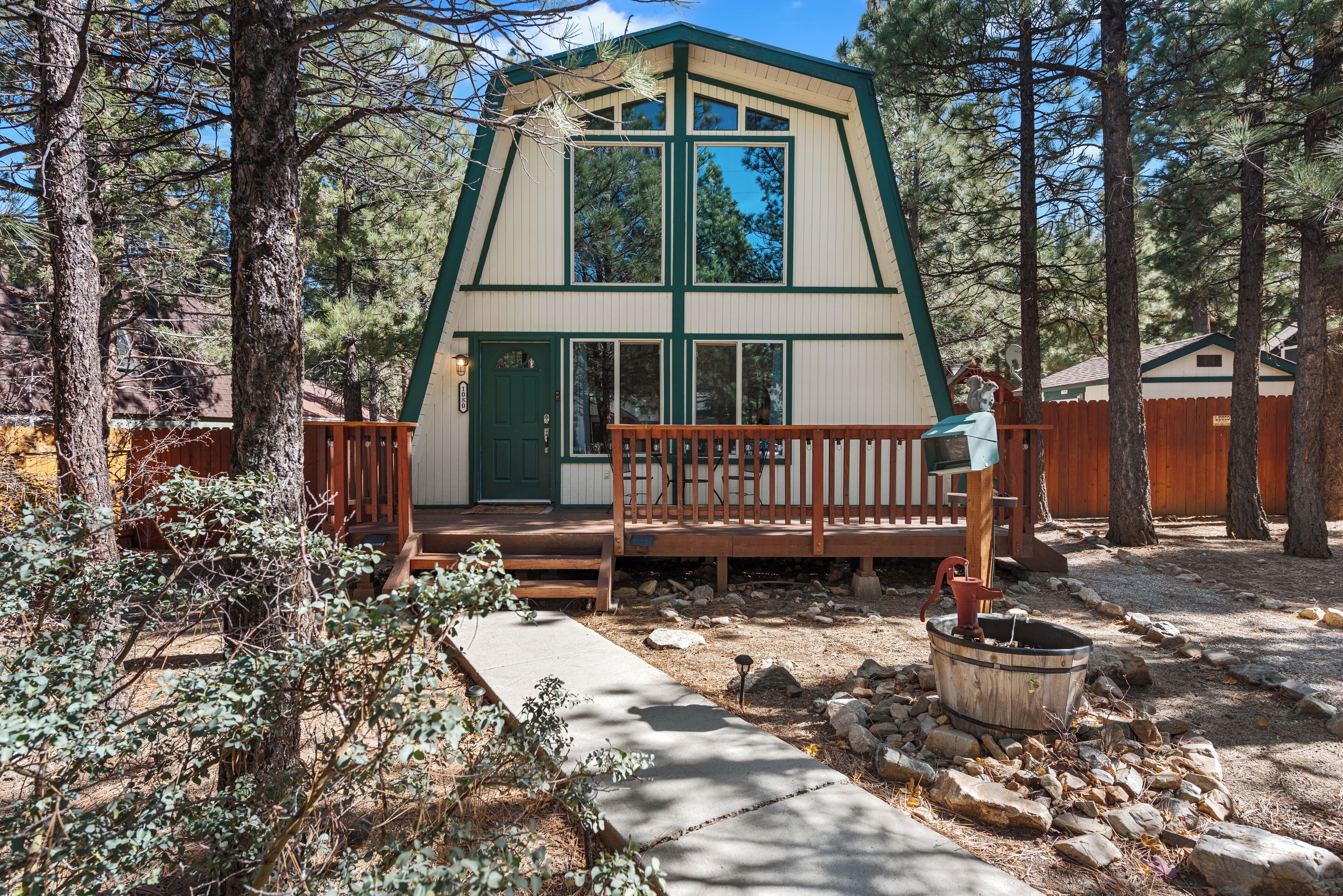 Una cabaña con terraza de madera, puerta verde y sendero de piedra.